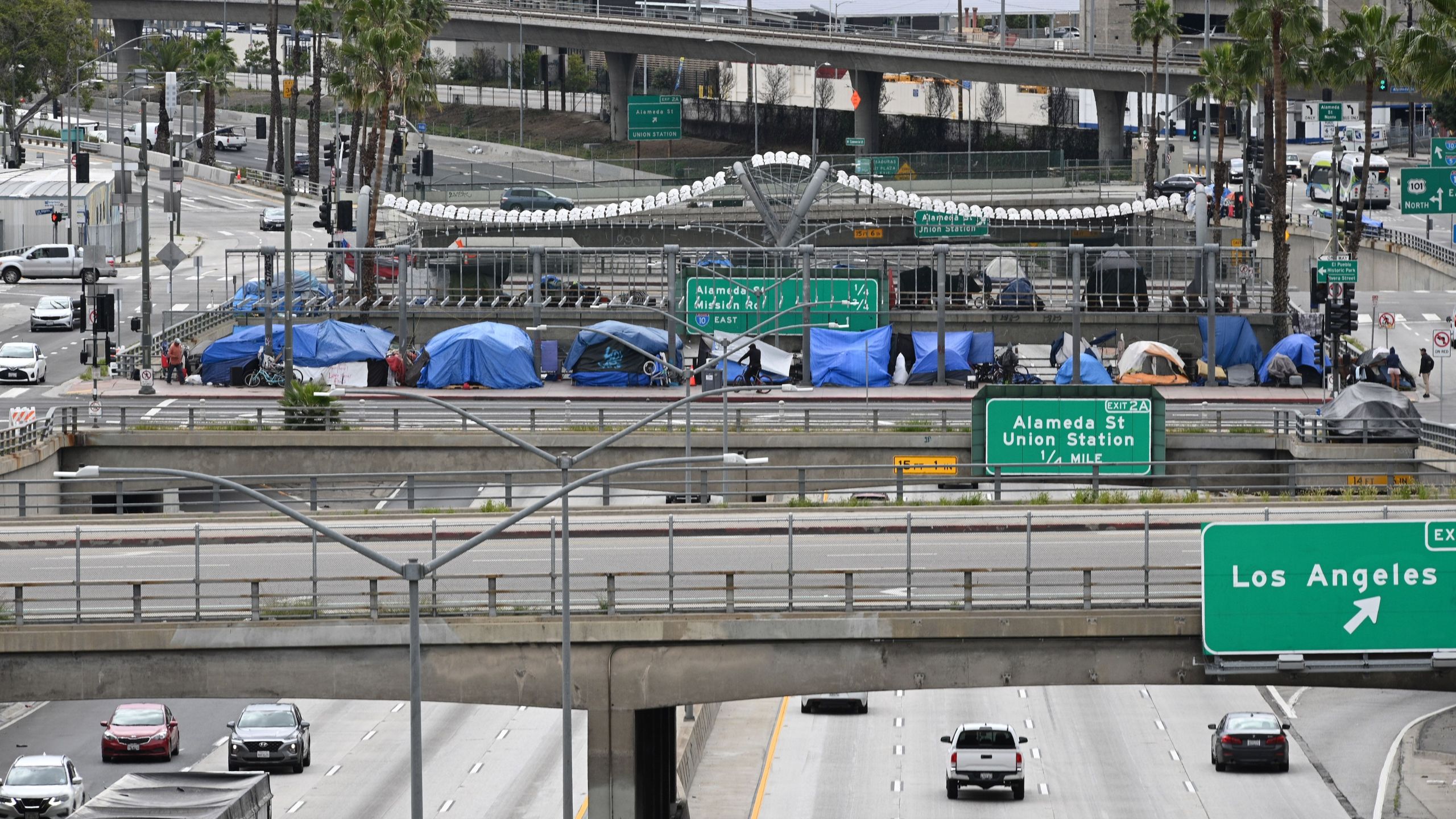 A man rides a bicycle in front of a row of homeless tents above a freeway on April 7, 2020 in Los Angeles. (ROBYN BECK/AFP via Getty Images)