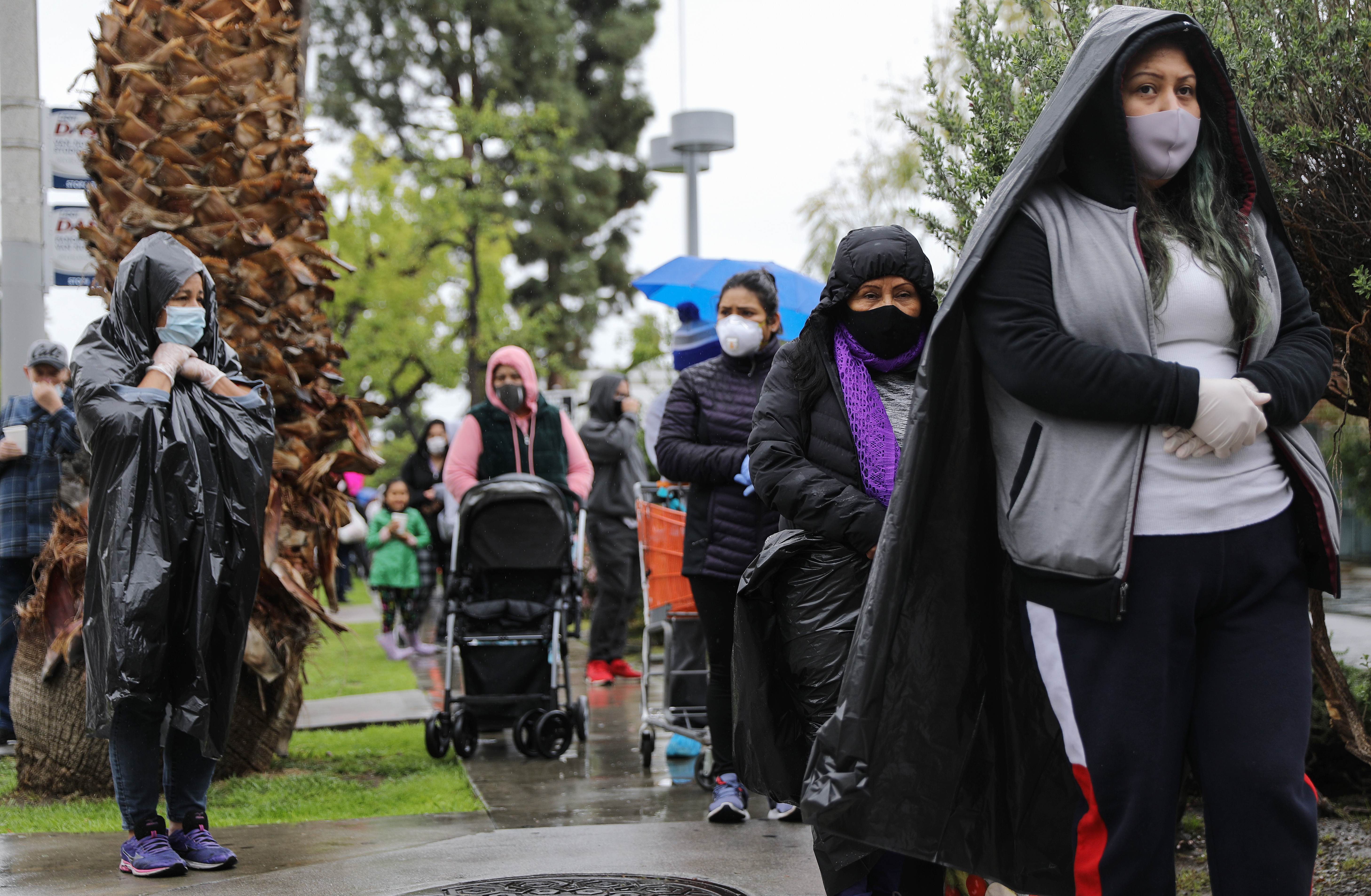 Juana Gomez, 50, from North Hollywood, wears a face mask and gloves, while using a trash bag to protect against the rain, as she waits in line to receive food at a Food Bank distribution for those in need as the coronavirus pandemic continues on April 9, 2020, in Van Nuys, Calif. (Mario Tama/Getty Images)