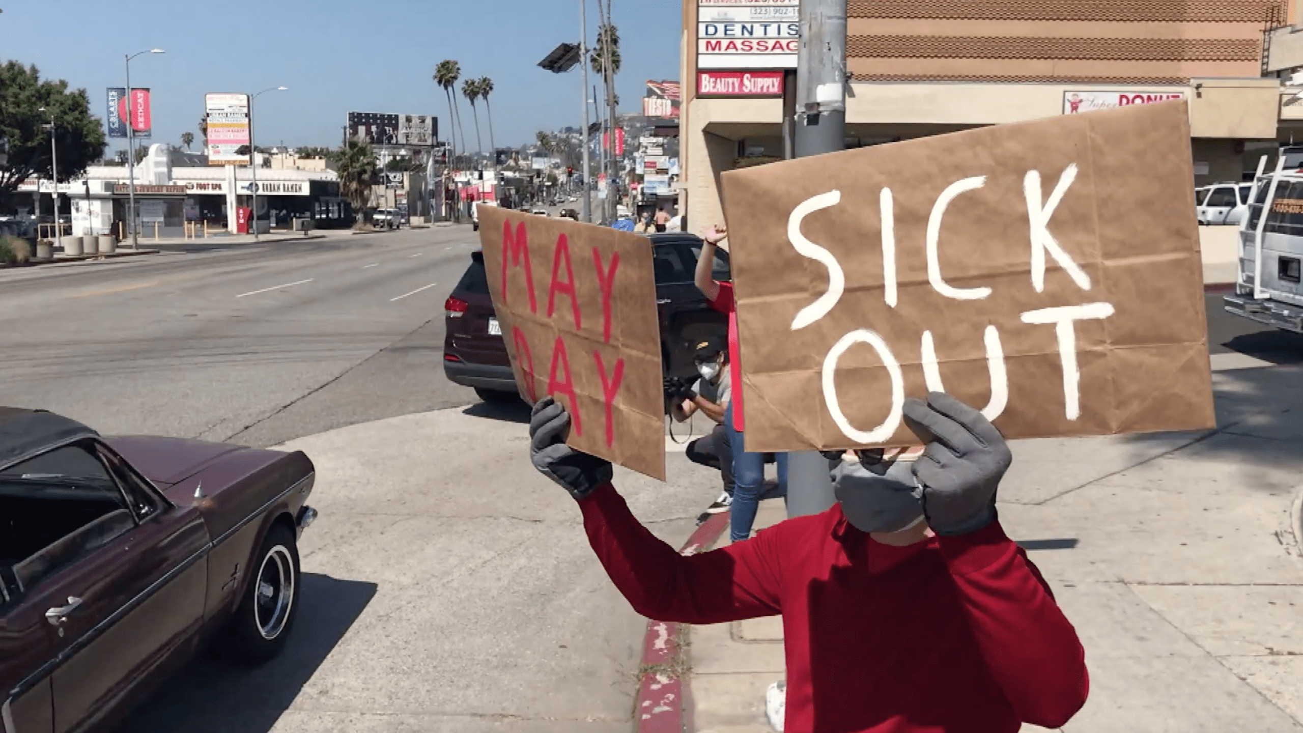 Protestors holds signs that read "May Day" and "Sick out" outside a Ralphs store in Hollywood on May 1, 2020. (KTLA)