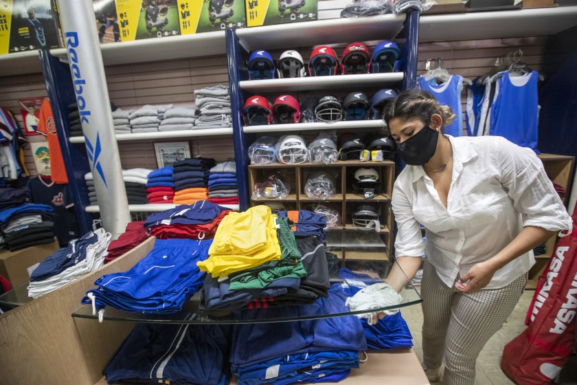 Daniela Prieto, an employee at Deportes Prieto in Boyle Heights, disinfects inside the store, which is currently allowing customers to preorder merchandise. The business reopened Monday for curbside pickup only.(Mel Melcon / Los Angeles Times)