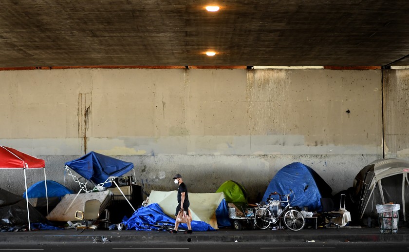 A man walks by a homeless encampment on Venice Boulevard under the 405 Freeway. A federal judge has ordered the city and county of Los Angeles to relocate thousands of homeless people living near freeways starting on Friday. (Wally Skalij/Los Angeles Times)