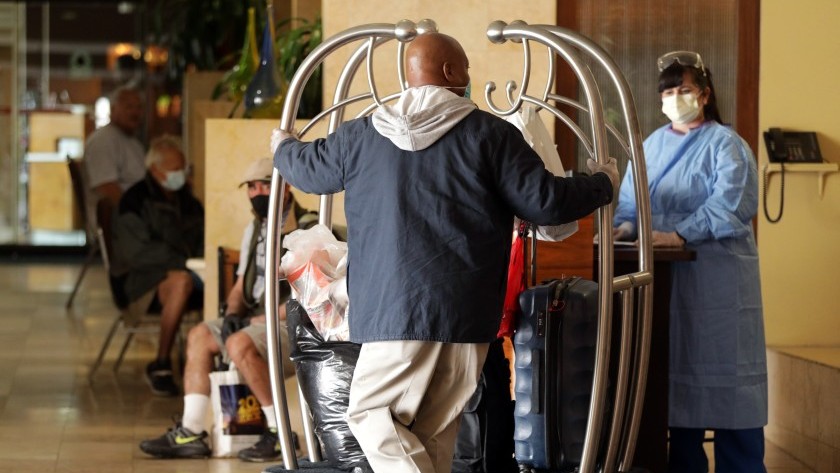 Omar Spry of Los Angeles Housing + Community Investment Department pushes a cart of residents’ bags into a West L.A. hotel that has been turned into housing for homeless people during the coronavirus outbreak.(Myung J. Chun / Los Angeles Times)