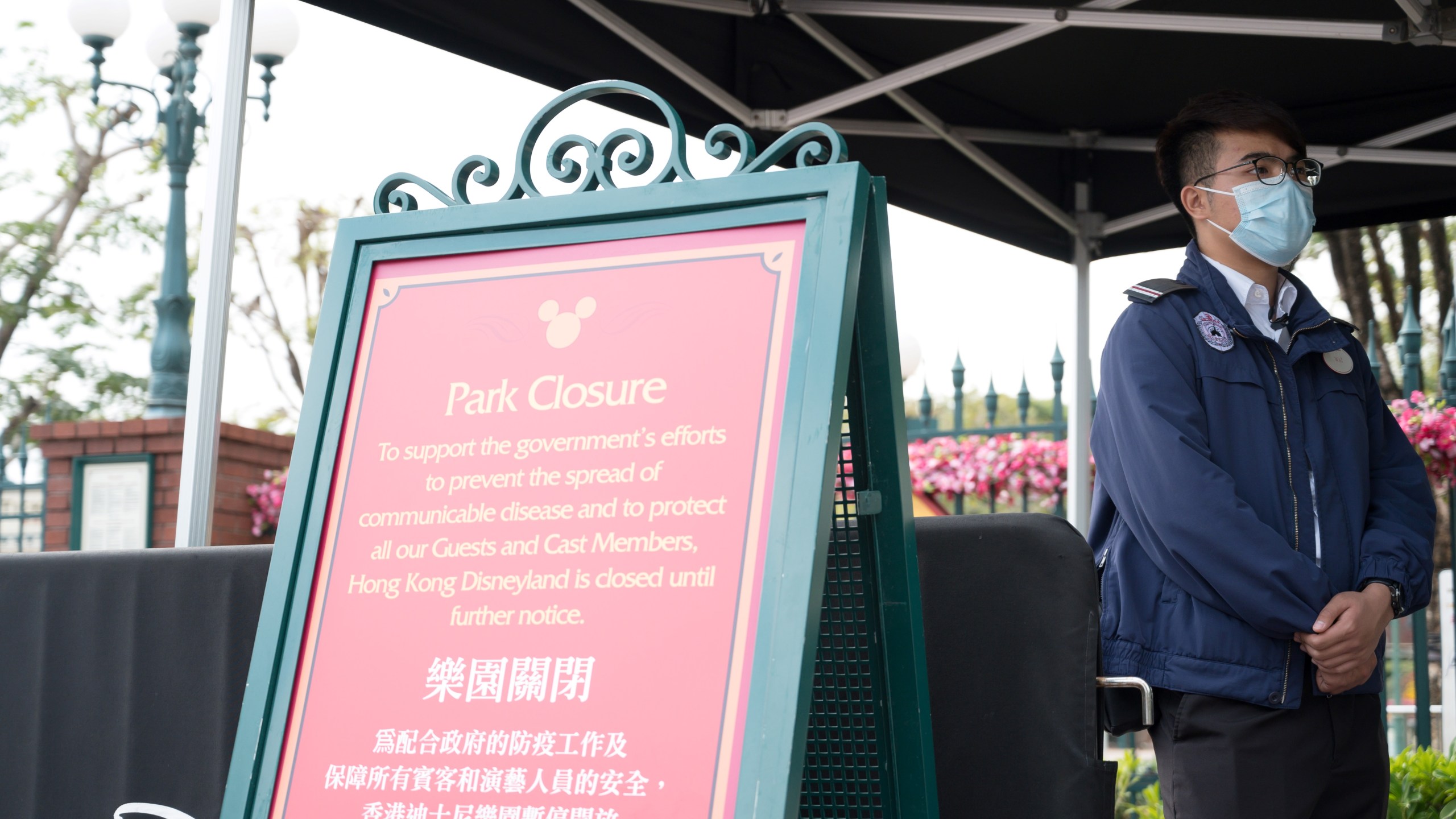 A member of staff wearing a mask stands next to a sign announcing the park's closure at Hong Kong Disneyland in Hong Kong on January 26, 2020, after it announced it was shutting its doors until further notice over a deadly virus outbreak in central China. (Ayaka MCGILL / AFP/Getty Images)