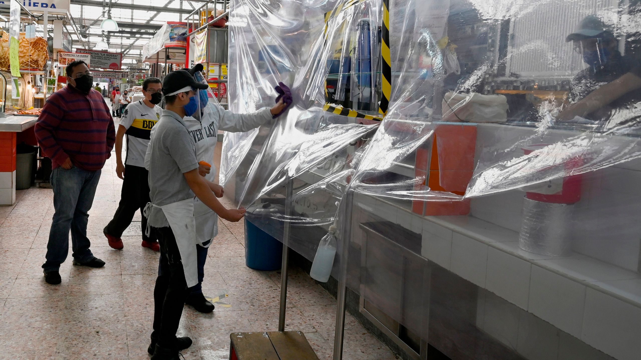 Two workers clean the plastic protection of a store to prevent the spread of COVID-19 at the Martinez de la Torre Market in Mexico City on May 28, 2020. (ALFREDO ESTRELLA/AFP via Getty Images)