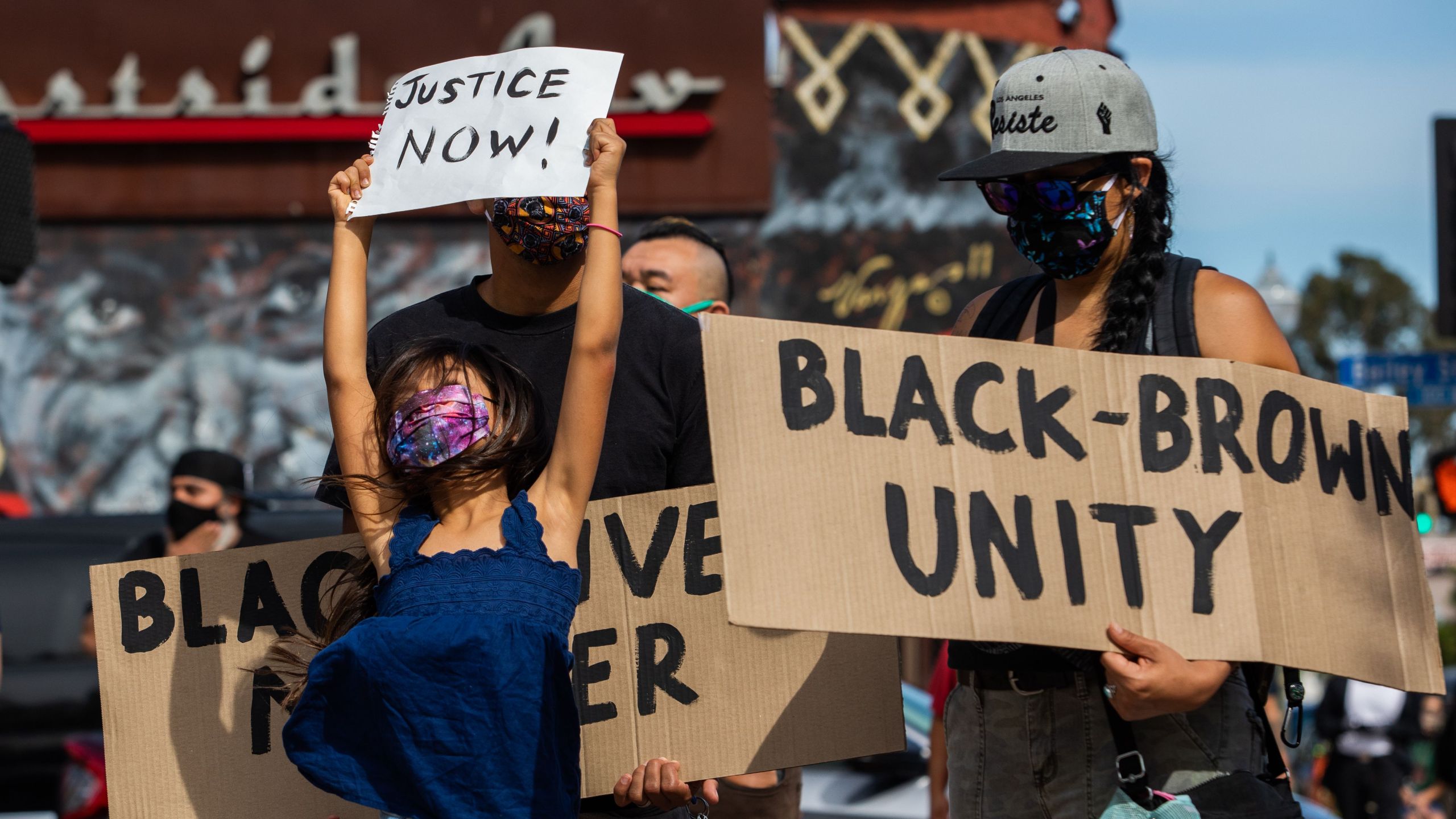 A girl jumps holding a sign that reads "Justice Now!" while she and her family protest in the Boyle Heights neighborhood of Los Angeles on May 30, 2020. (APU GOMES/AFP via Getty Images)