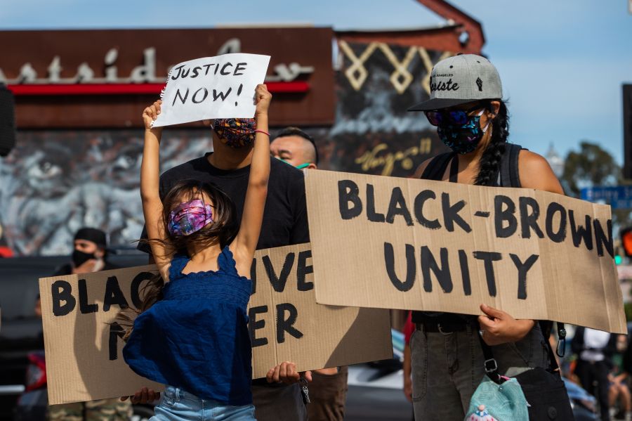 A girl jumps holding a sign that reads "Justice Now!" while she and her family protest in the Boyle Heights neighborhood of Los Angeles on May 30, 2020. (APU GOMES/AFP via Getty Images)