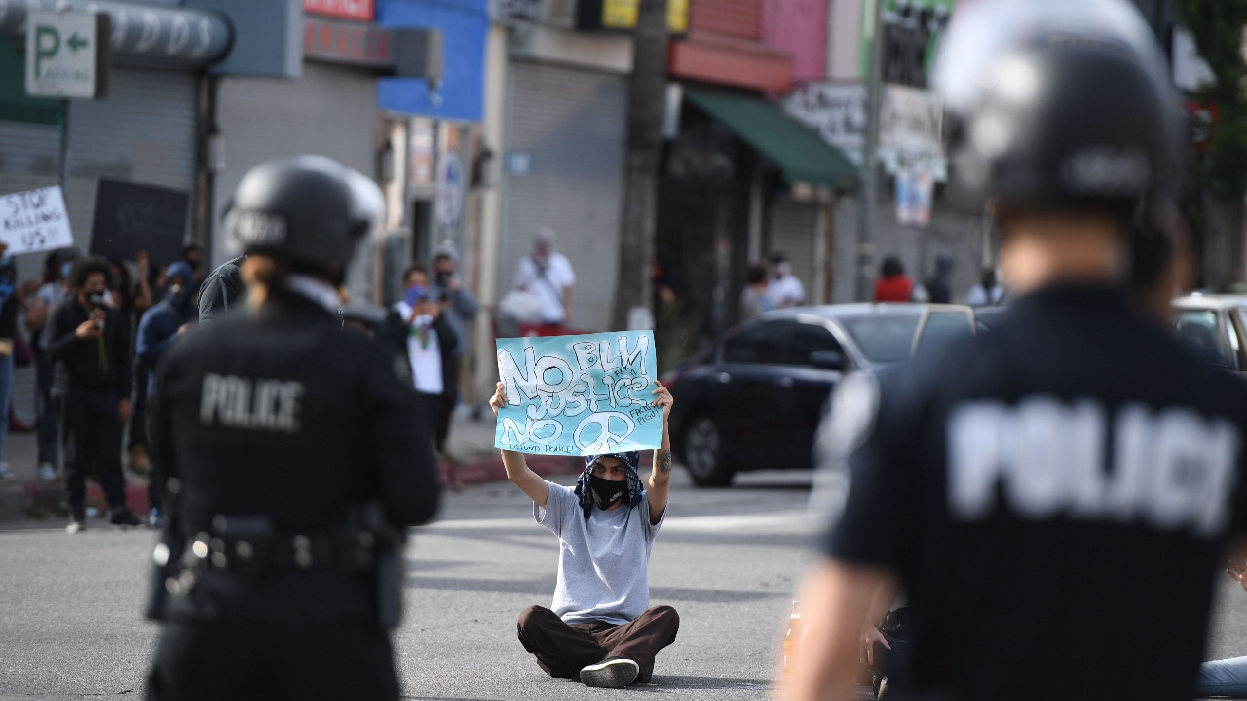 A demonstrator holds a sign as he sits in front of police in Van Nuys on June 1, 2020. (Robyn Beck / AFP / Getty Images)