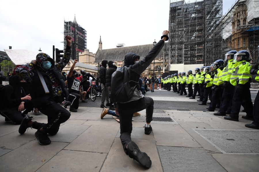 Protesters kneel and raise their fists in the air as police officers line up outside the Houses of Parliament during a Black Lives Matter protest in Westminster on June 7, 2020 in London, United Kingdom. (Chris J Ratcliffe/Getty Images)