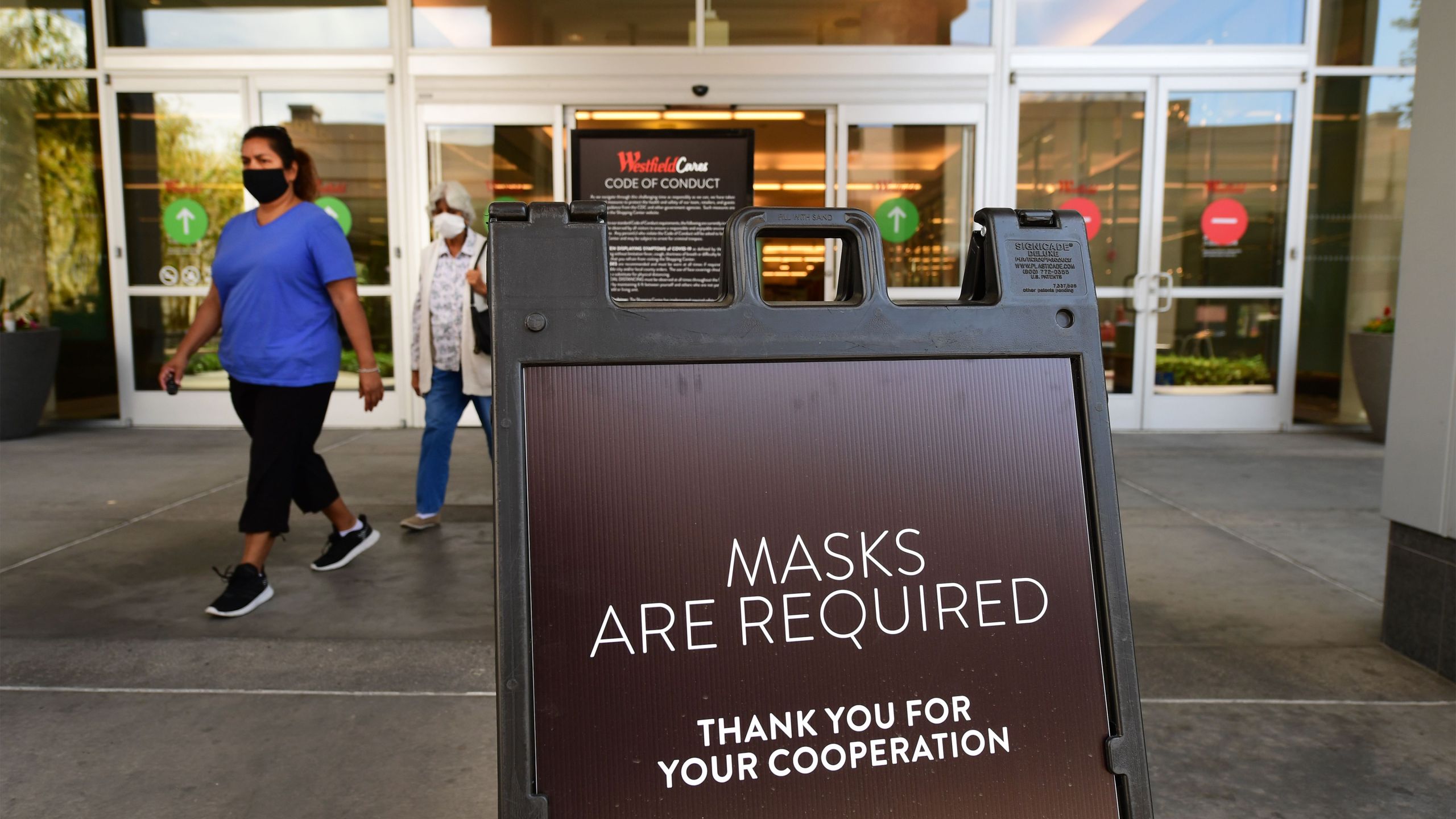 Women wearing face masks exit a shopping mall where a sign is posted at an entrance reminding people of the mask requirement at Westfield Santa Anita mall in Arcadia on June 12, 2020. (FREDERIC J. BROWN/AFP via Getty Images)