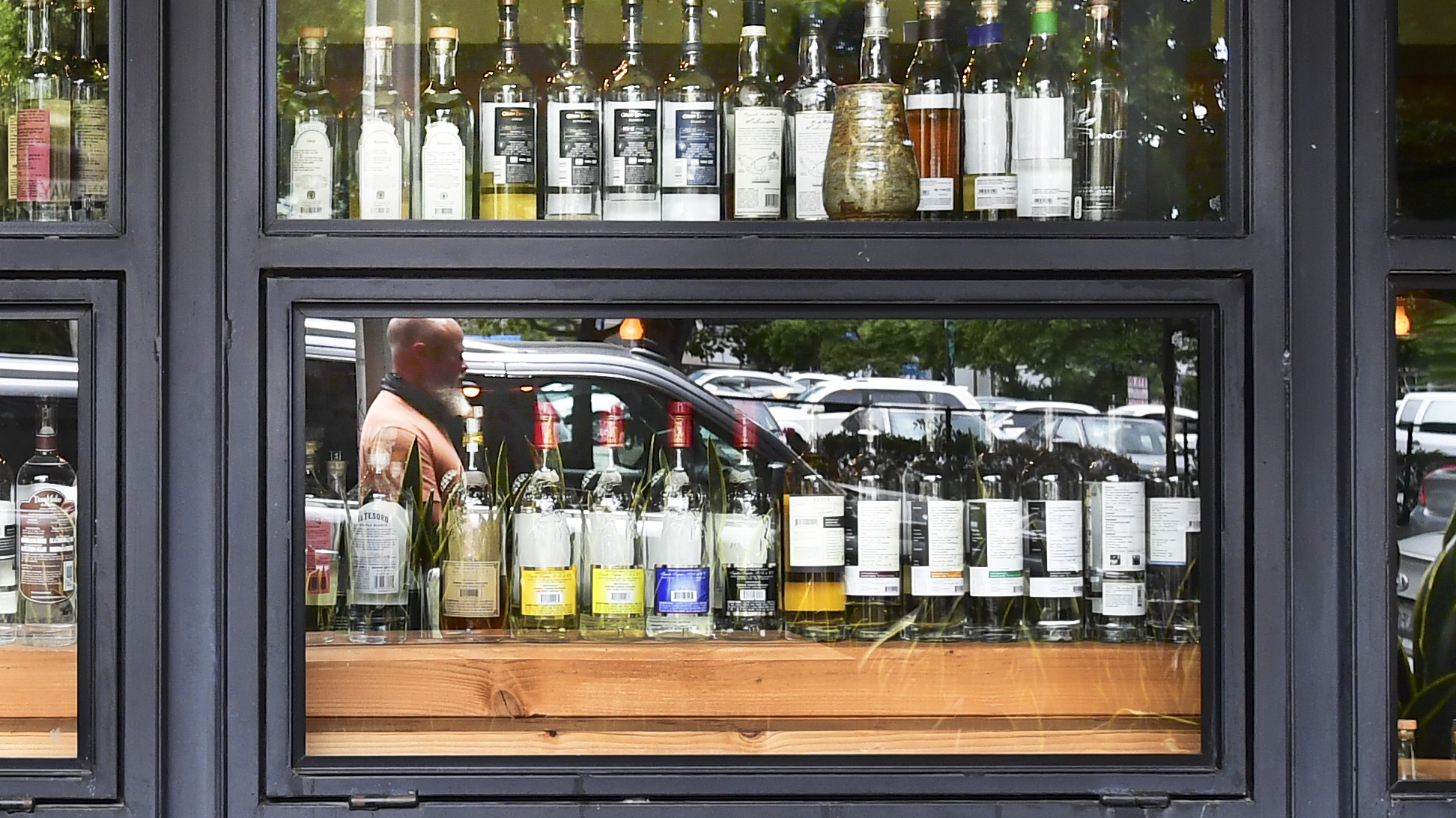 A pedestrian's reflection is seen while walking past bottles of liquor at a bar in Los Angeles on June 29, 2020. (Frederic J. Brown / AFP / Getty Images)