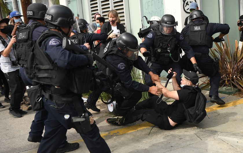 A Los Angeles police officer holds a so-called less-lethal projectile launcher as fellow officers arrest a protester during a demonstration in the Fairfax district in the summer of 2020. (Wally Skalij/Los Angeles Times)