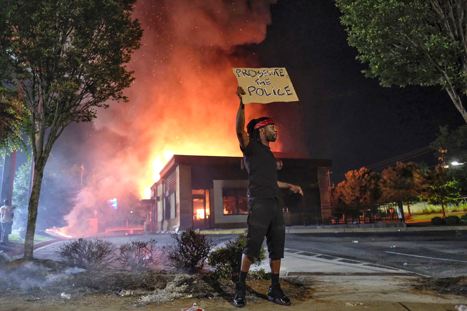 A person holds a sign as a Wendy's restaurant burns Saturday, June 13, 2020, in Atlanta after demonstrators protesting the death of Rayshard Brooks set it on fire. (Ben GrayAtlanta Journal-Constitution via AP/ CNN)