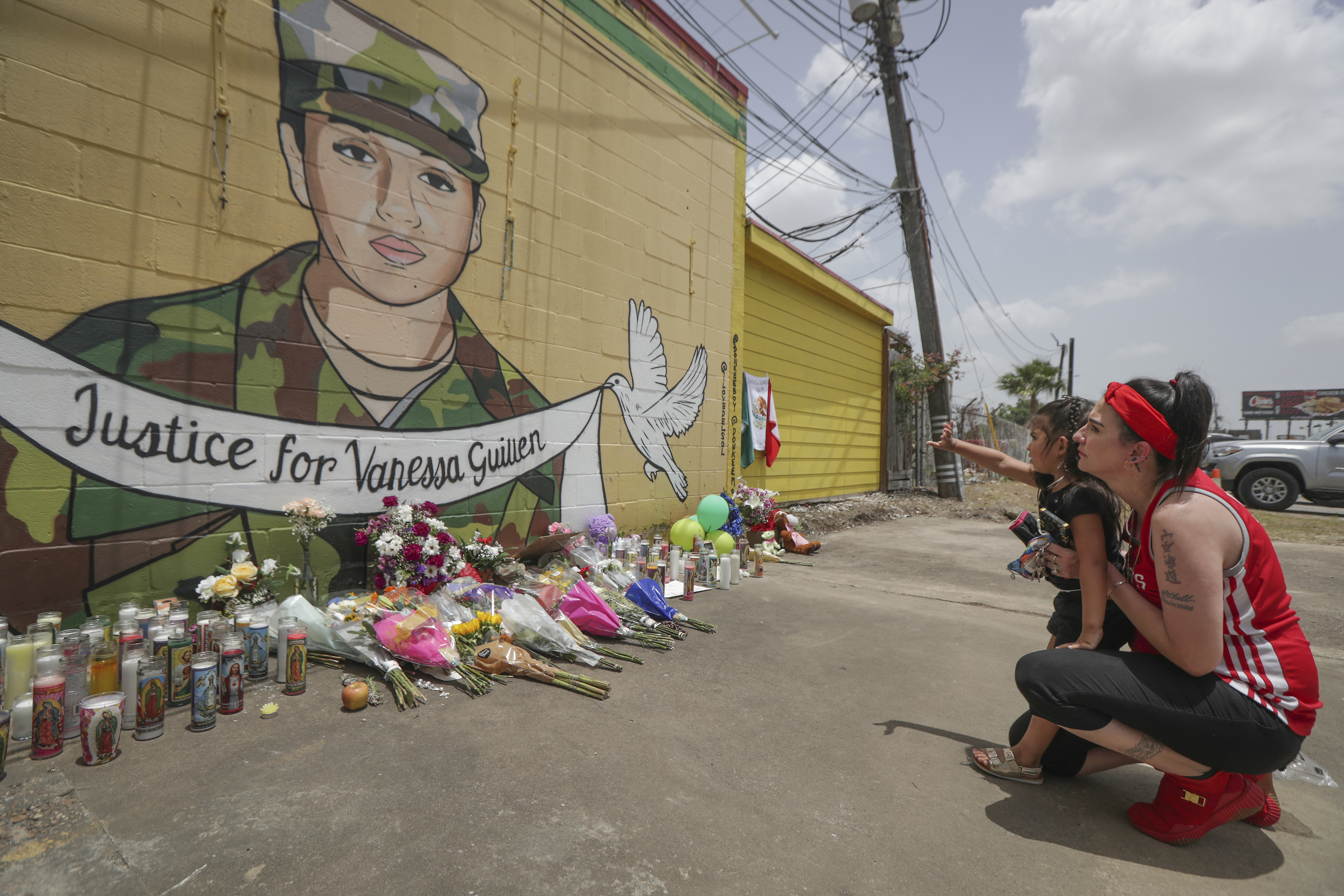 Dawn Gomez holds her 3-year-old granddaughter, Saryia Greer, who waves at Vanessa Guillen's mural painted by Alejandro "Donkeeboy" Roman Jr. on the side of Taqueria Del Sol, Thursday, July 2, 2020, in Houston. Army investigators believe Guillen, a Texas soldier missing since April, was killed by another soldier on the Texas base where they served, the attorney for the missing soldier's family said Thursday. (Steve Gonzales/Houston Chronicle via AP)