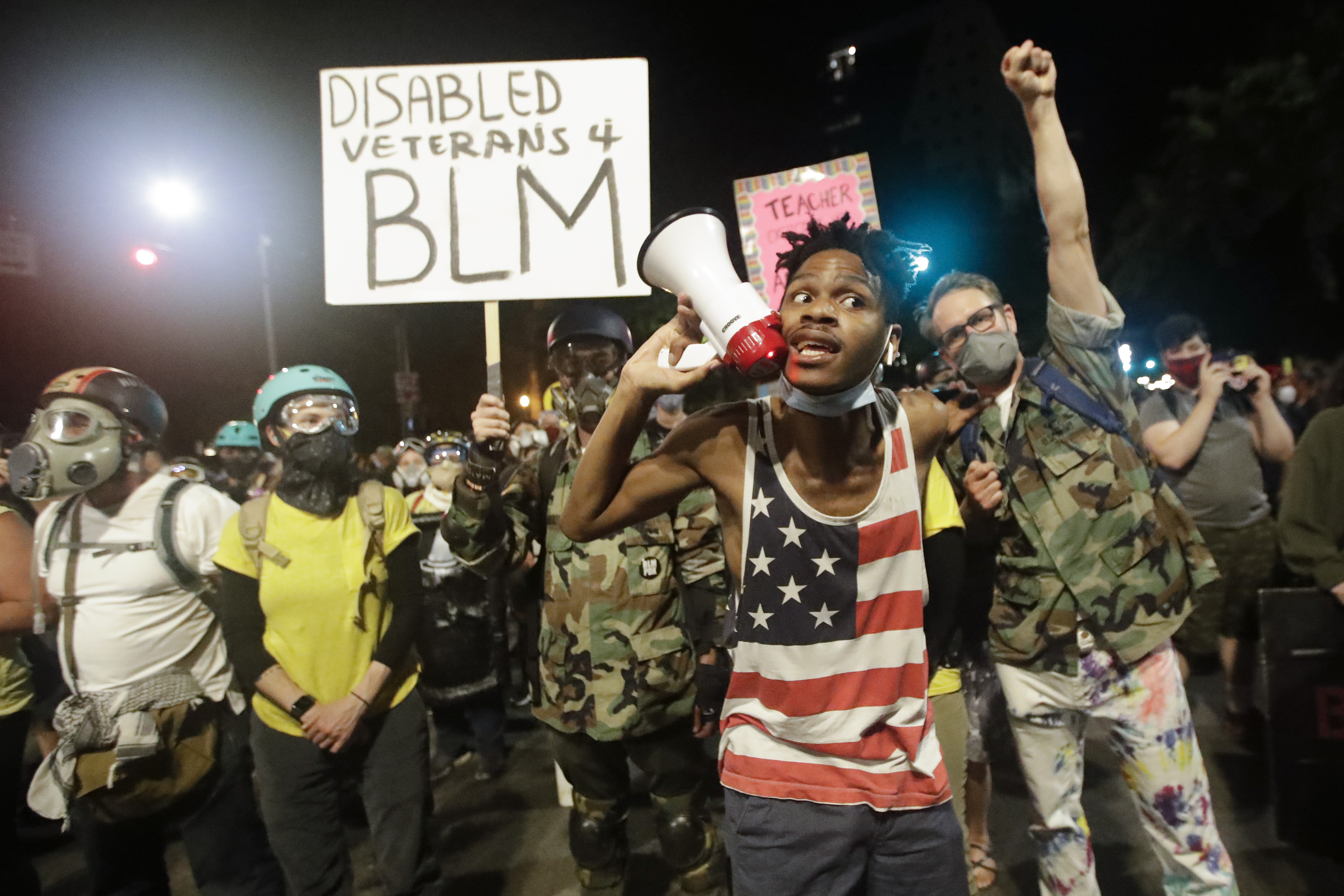 A demonstrator shouts slogans using a bullhorn next to a group of military veterans during a Black Lives Matter protest at the Mark O. Hatfield United States Courthouse Sunday, July 26, 2020, in Portland, Ore. (AP Photo/Marcio Jose Sanchez)