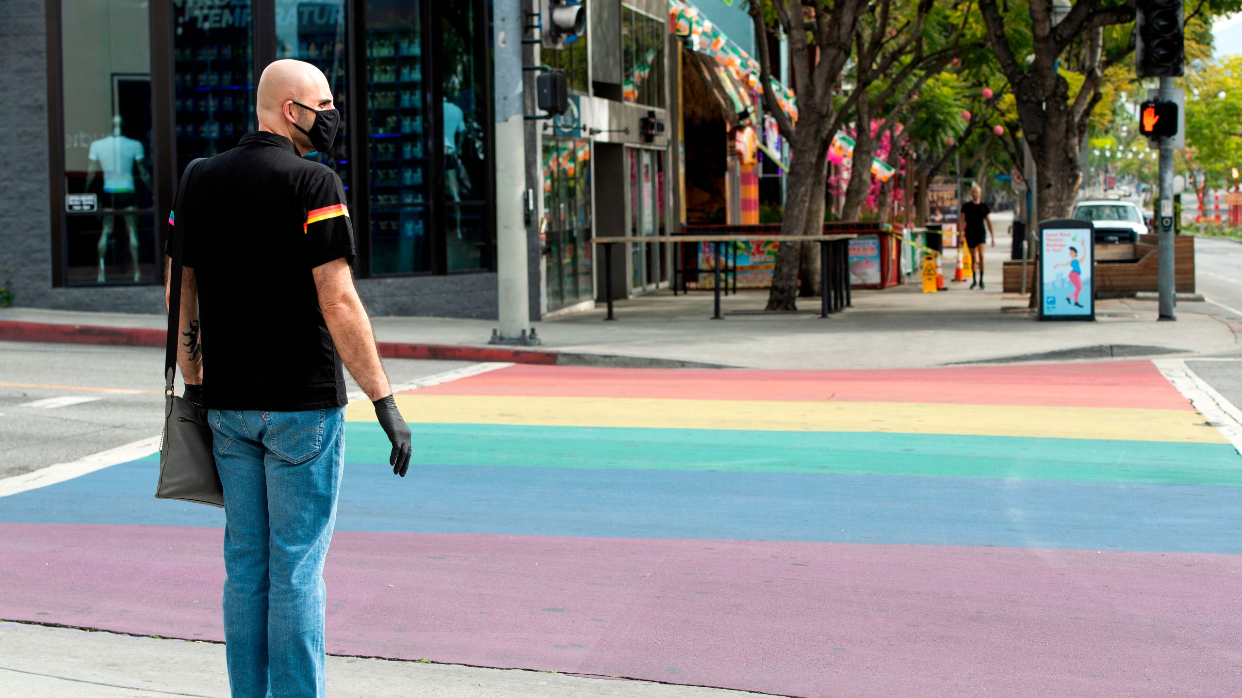 A person with a mask crosses an empty street in West Hollywood during stay-home orders on March 31, 2020. (VALERIE MACON / AFP / Getty Images)