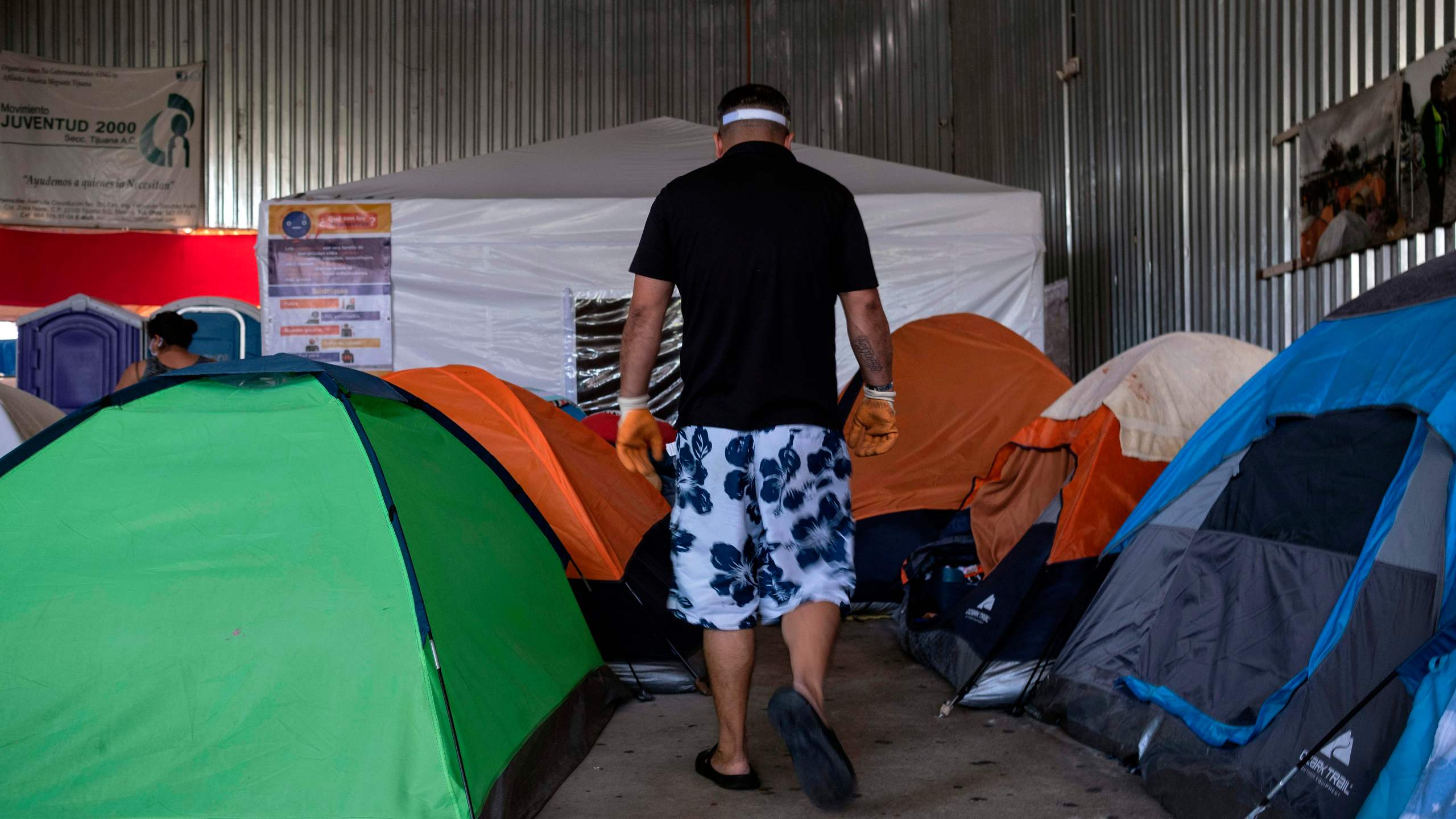 An asylum seeker walks among tents, with one in the background dedicated to people suspected to be infected with COVID-19, at the Juventud 2000 migrant shelter in Tijuana on June 19, 2020. (Guillermo Arias / AFP / Getty Images)