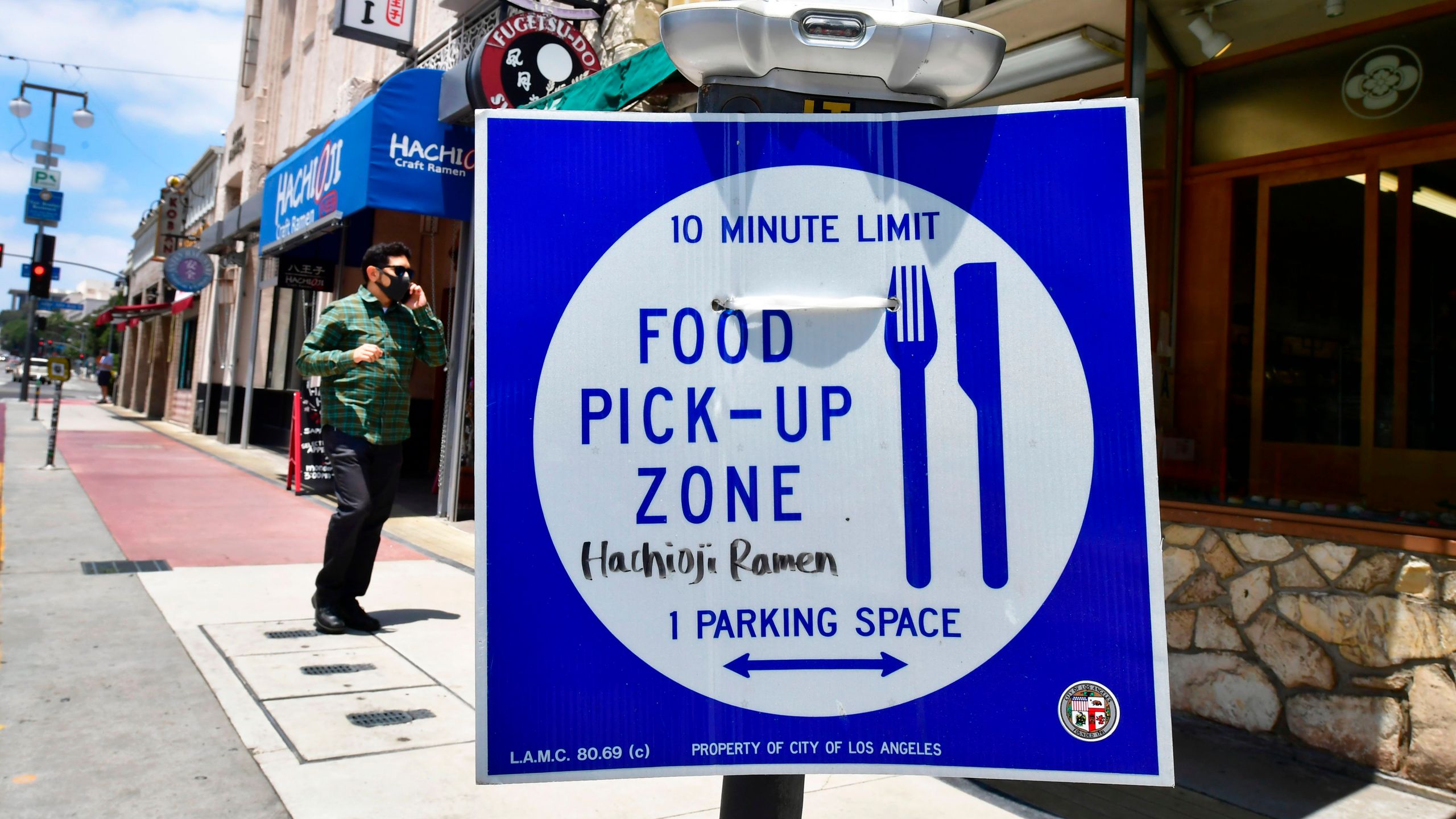 A pedestrian wearing a face mask walks past a sign for food pick-up outside a restaurant in Los Angeles on July 1, 2020, after indoor restaurants, bars and movie theaters across much of California were ordered to close for at least three weeks. (FREDERIC J. BROWN/ Getty Images)