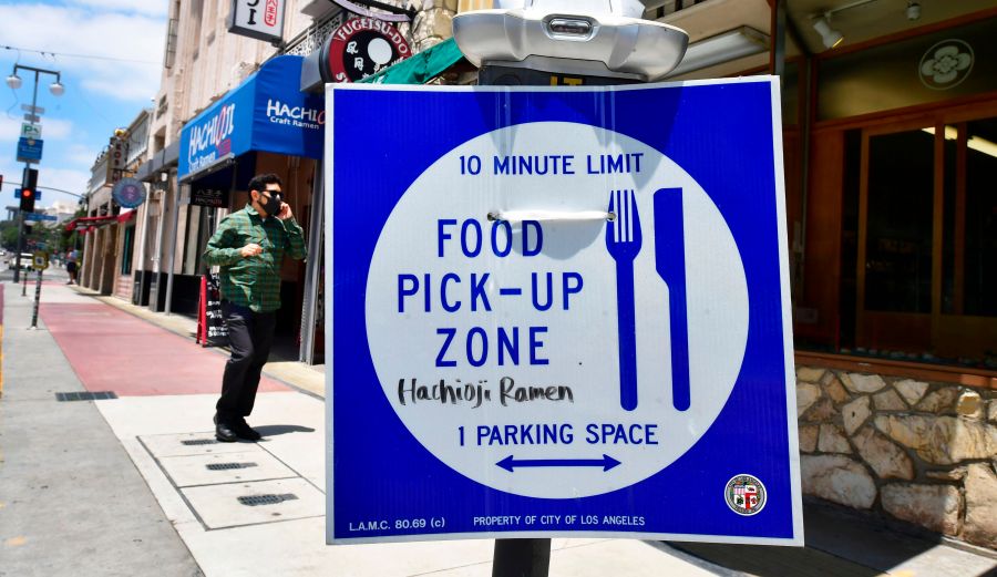 A pedestrian wearing a face mask walks past a sign for food pick-up outside a restaurant in Los Angeles on July 1, 2020, after indoor restaurants, bars and movie theaters across much of California were ordered to close for at least three weeks. (FREDERIC J. BROWN/ Getty Images)