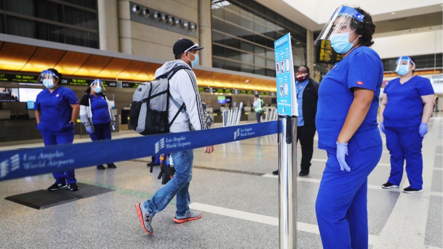 LOS ANGELES, CALIFORNIA - JUNE 24: A traveler walks past screeners testing a system of thermal imaging cameras which check body temperatures at Los Angeles International Airport (LAX) amid the COVID-19 pandemic on June 24, 2020 in Los Angeles, California. The system is being tested in the international terminal for twelve weeks and can flag passengers who have a fever, one of the symptoms of the coronavirus. (Photo by Mario Tama/Getty Images)