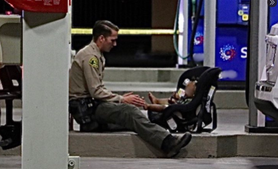 A sheriff's deputy sits with a 1-year-old at the scene of a shooting in Lancaster on July 15, 2020. (Los Angeles County Sheriff's Department)