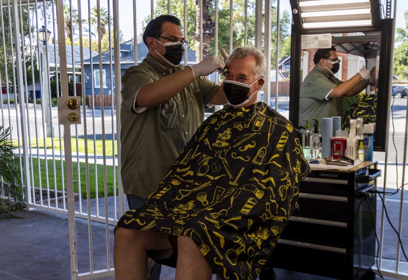 Obie Figueroa, owner of Obie’s Barbershop & Shave in Riverside, cuts San Dimas resident Matt Nelson’s hair Tuesday. The coronavirus pandemic has forced Figueroa to move his services outside.(Gina Ferazzi / Los Angeles Times)