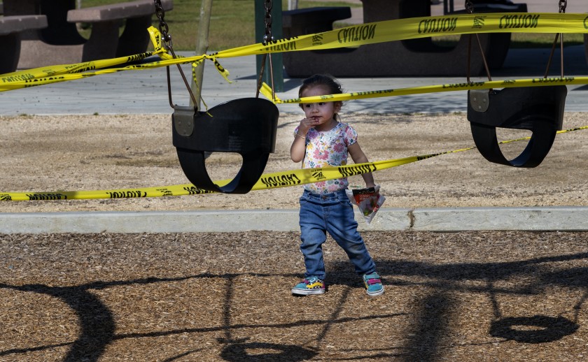 Adeline Hernandez, 2, of Riverside seems perplexed by the yellow caution tape as she approaches the closed off swing sets at Ryan Bonaminio Park during the COVID-19 pandemic in April 2020. (Gina Ferazzi / Los Angeles Times)