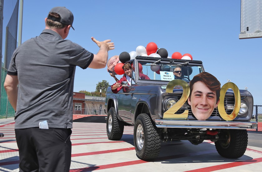 Graduate Dylan Davis is congratulated by coach John Shanahan as he exits the Laguna Beach High drive-through graduation at Guyer Field in 2020. (Don Leach / Times Community News)