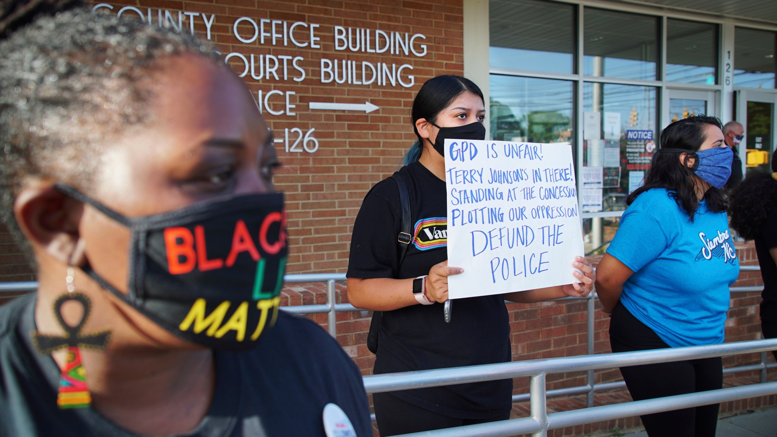 Aranza Sosa, center, holds a sign at a protest in front of the Alamance County government building in Graham, N.C., on Monday, Aug. 3, 2020. Sosa, who was born in Mexico and is now a U.S. citizen, says the county is a hostile place for people of color. (AP Photo/Allen G. Breed)