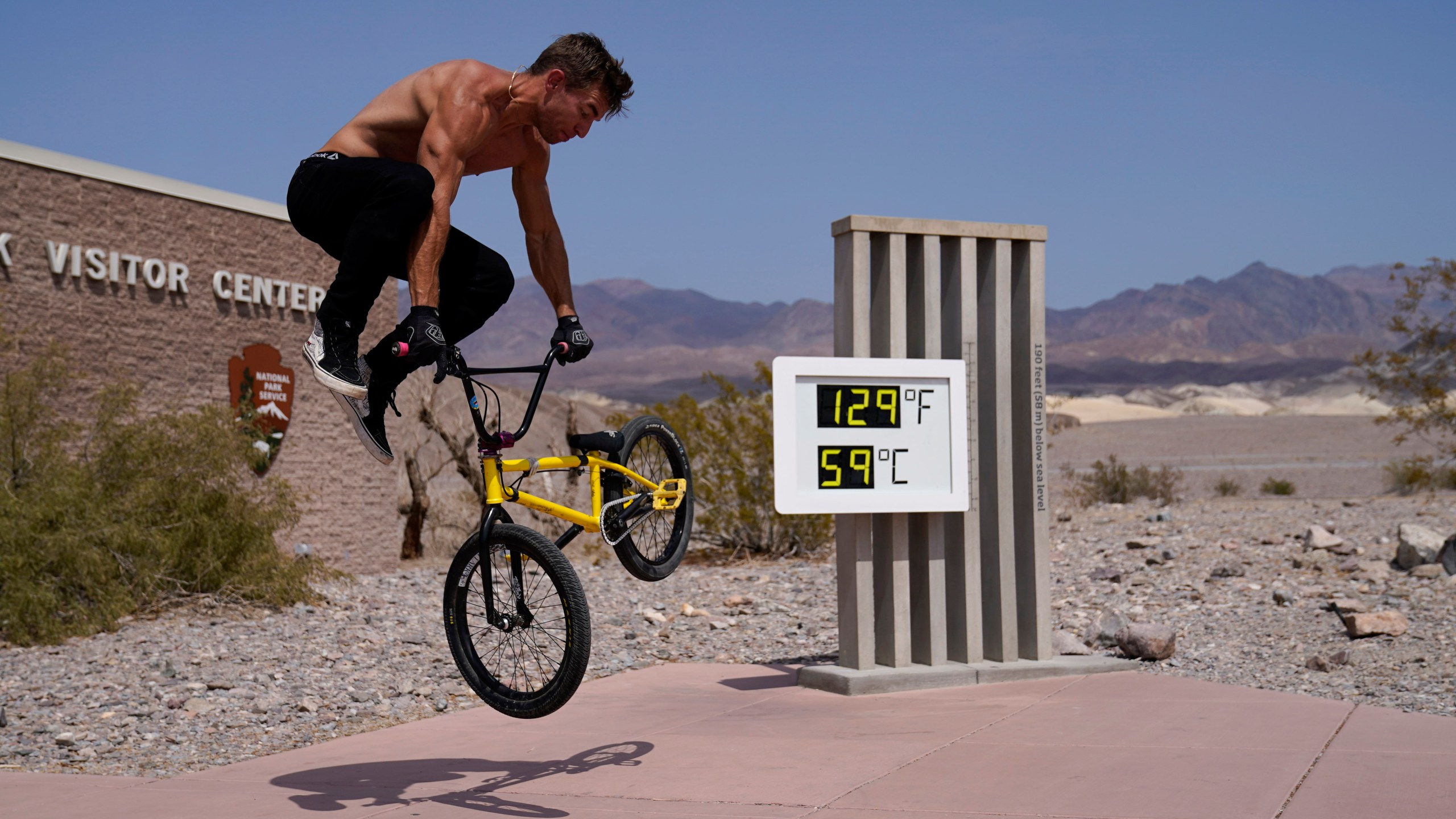 Michael Major rides his bike at the Furnace Creek Visitor Center thermometer Monday, Aug. 17, 2020, in Death Valley National Park, Calif. The thermometer is not official but is a popular photo spot. (AP Photo/John Locher)