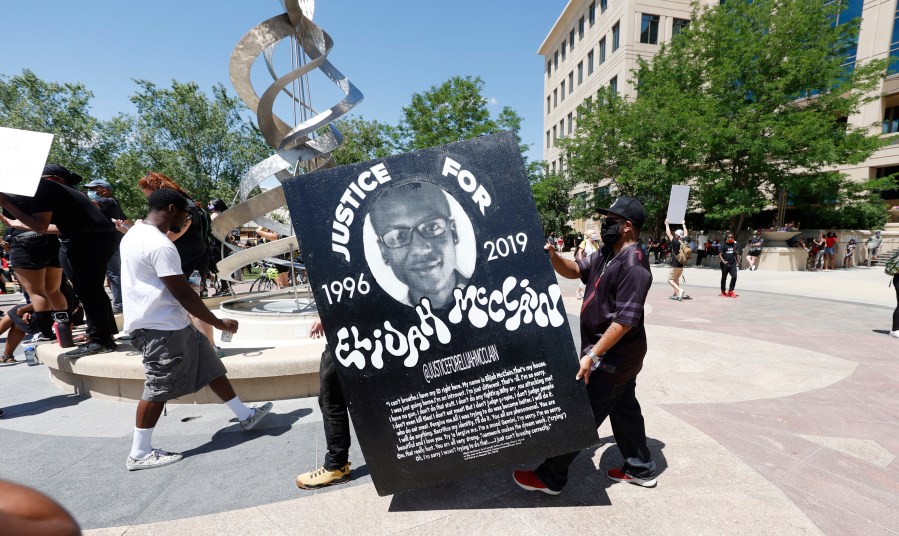 In this June 27, 2020 photo, demonstrators carry a giant placard during a rally and march over the death of 23-year-old Elijah McClain outside the police department in Aurora, Colorado. (AP Photo/David Zalubowski, File)