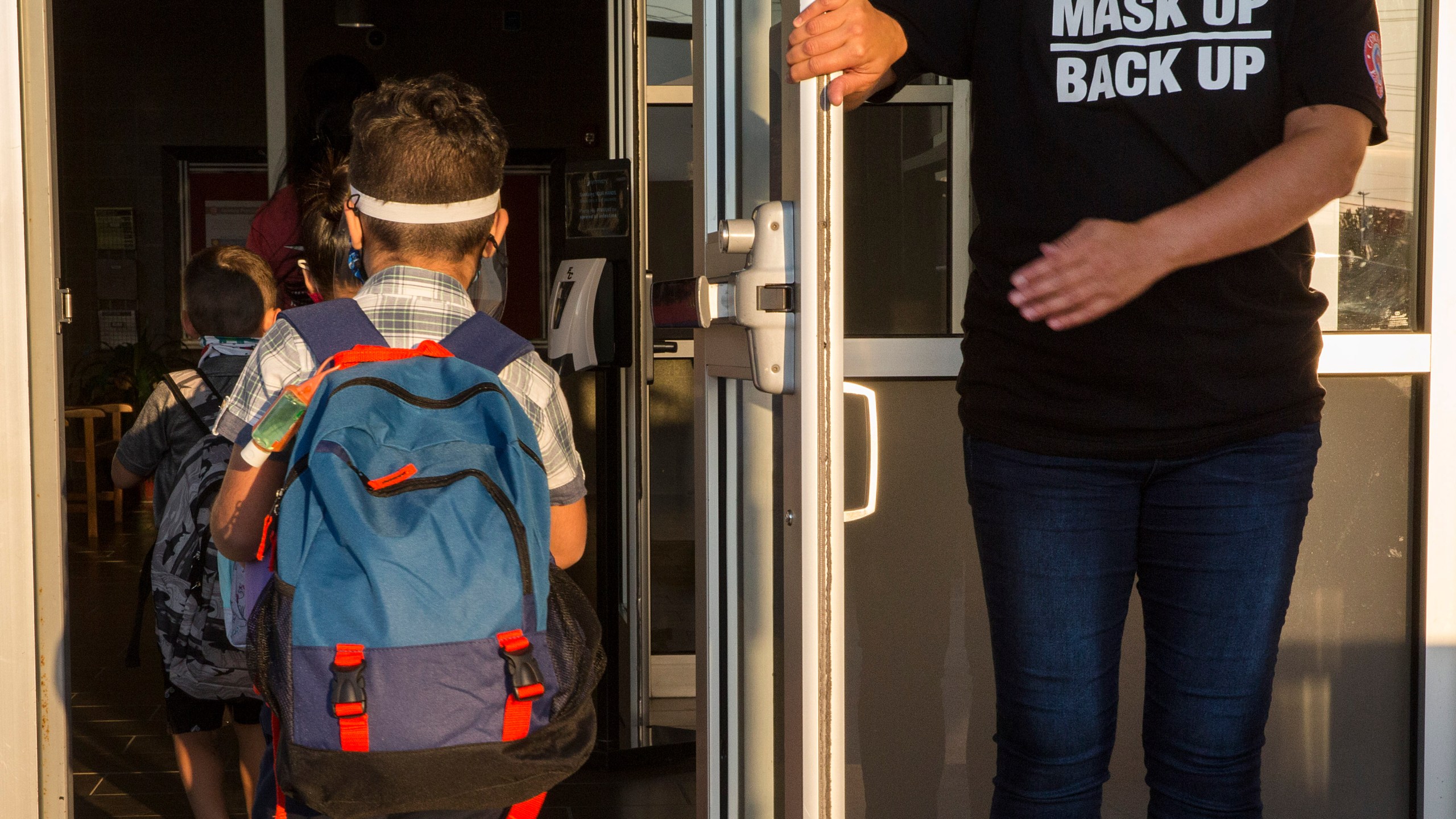 A staff member holds the door open for kids on the first day of school at Goodwin Frazier Elementary School in New Braunfels, Texas on Tuesday, Aug. 25, 2020. The number of Americans newly diagnosed with the coronavirus is falling — a development experts credit at least partly to increased wearing of masks — even as the outbreak continues to claim nearly 1,000 lives in the U.S. each day. (Mikala Compton/Herald-Zeitung via AP)