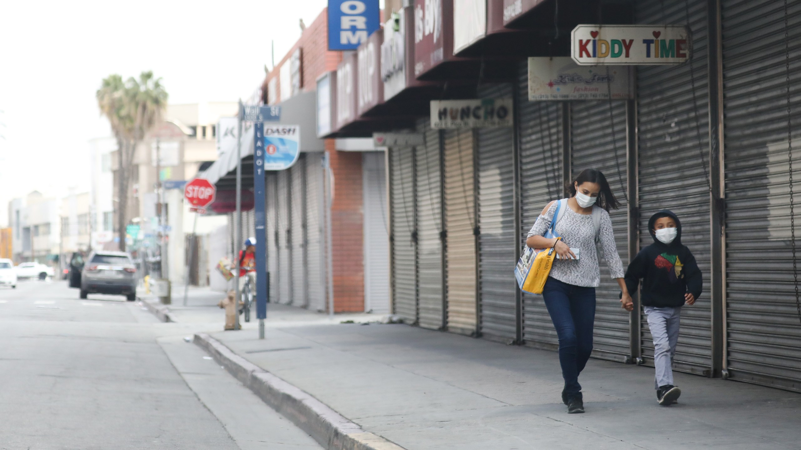 A woman and child wear face masks while walking past shuttered downtown shops amid the coronavirus pandemic on April 4, 2020 in Los Angeles. (Mario Tama/Getty Images)