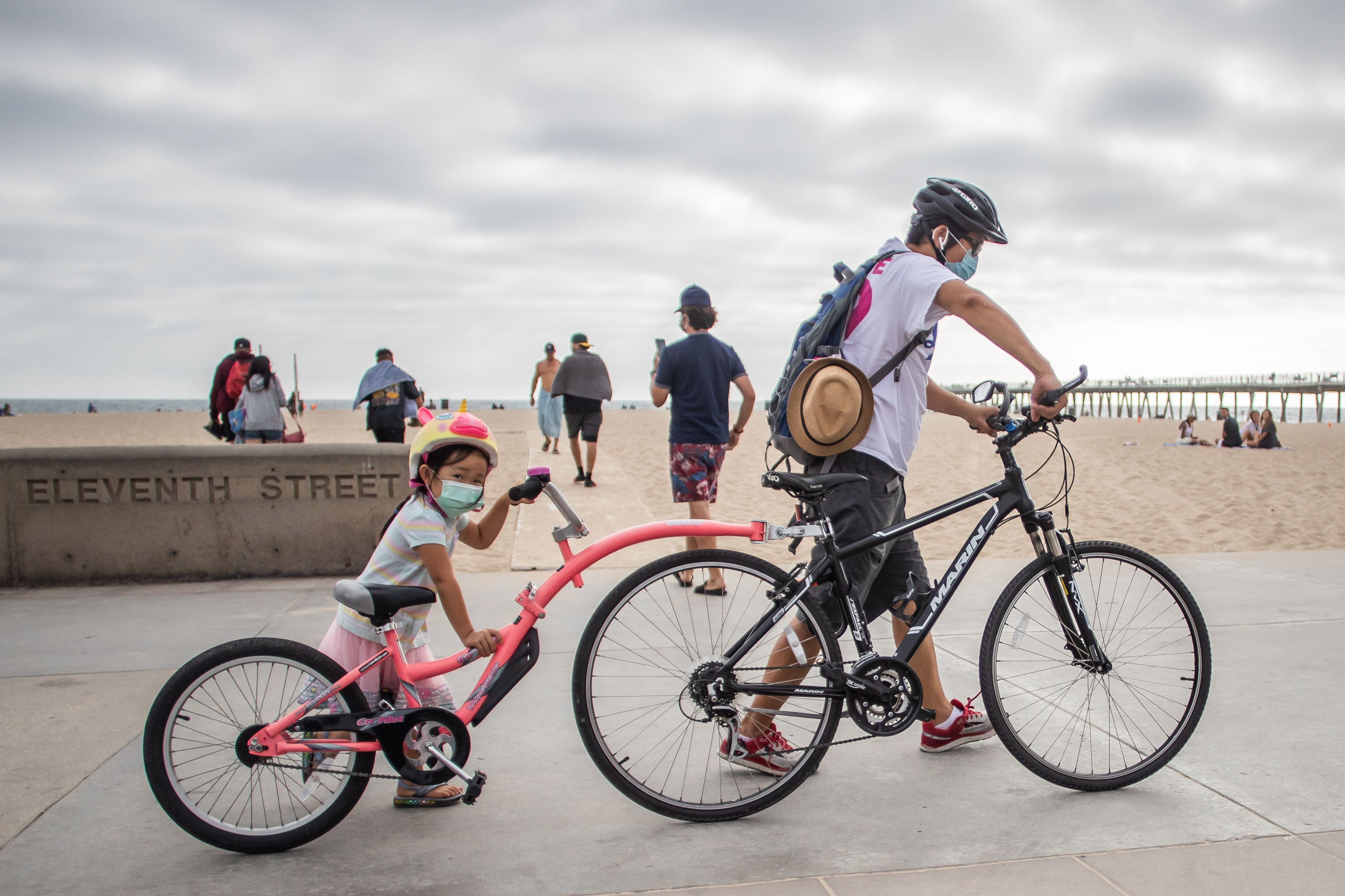 A girl and her father wear facemasks while they push their bikes in Hermosa Beach on July 14, 2020. (Apu GOMES / AFP via Getty Images)