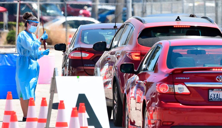 A volunteer dressed in personal protective equipment gestures to a driver in line at a coronavirus test site on July 30, 2020, in the Panoramic City neighborhood of Los Angeles. (FREDERIC J. BROWN/AFP via Getty Images)