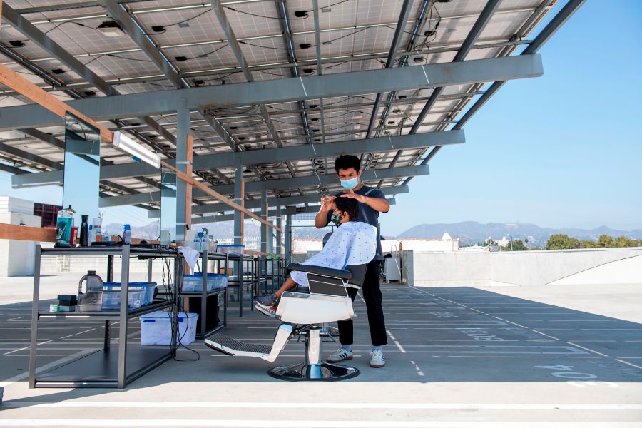 A stylist from Grey Matter LA cuts a young client's hair on a roof top parking lot amid the novel coronavirus pandemic, Aug. 4, 2020, in Los Angeles. (Valerie Macon / AFP / Getty Images)