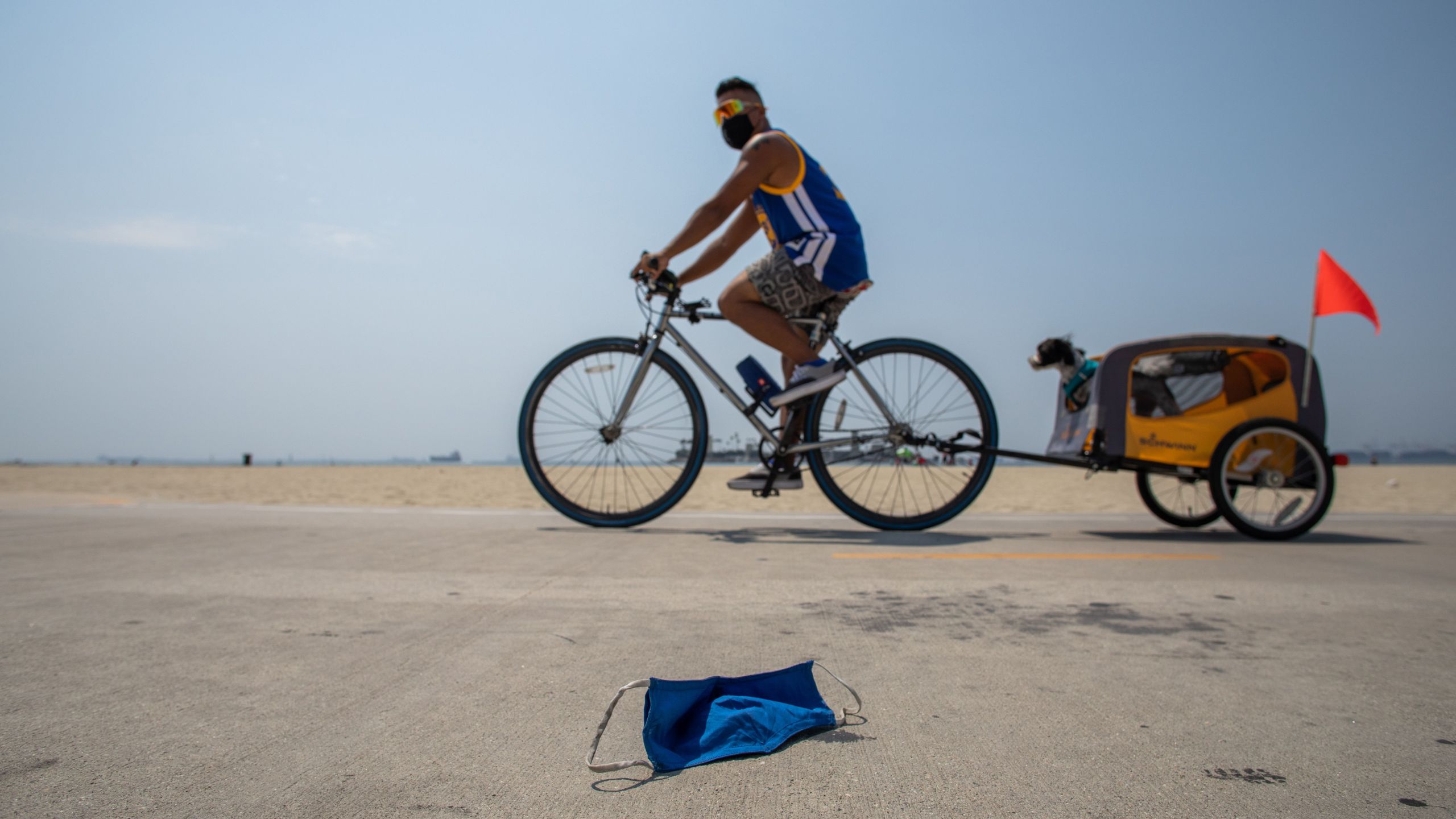 A man wearing a face mask rides his bike next to a discarded face mask in the bike path in Long Beach on Aug. 22, 2020.(APU GOMES/AFP via Getty Images)