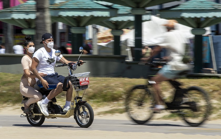 People wear protective masks while riding on the bicycle path in Venice Beach on Sunday.(Mel Melcon / Los Angeles Times)