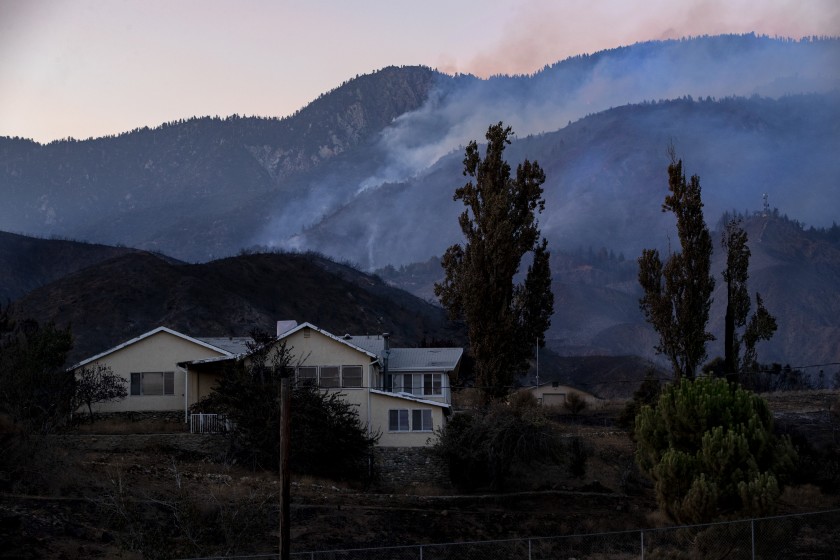 Scorched terrain surrounds a home off Bluff Street as the Apple fire smolders in the background on Tuesday in Banning, Calif.(Gina Ferazzi/Los Angeles Times)