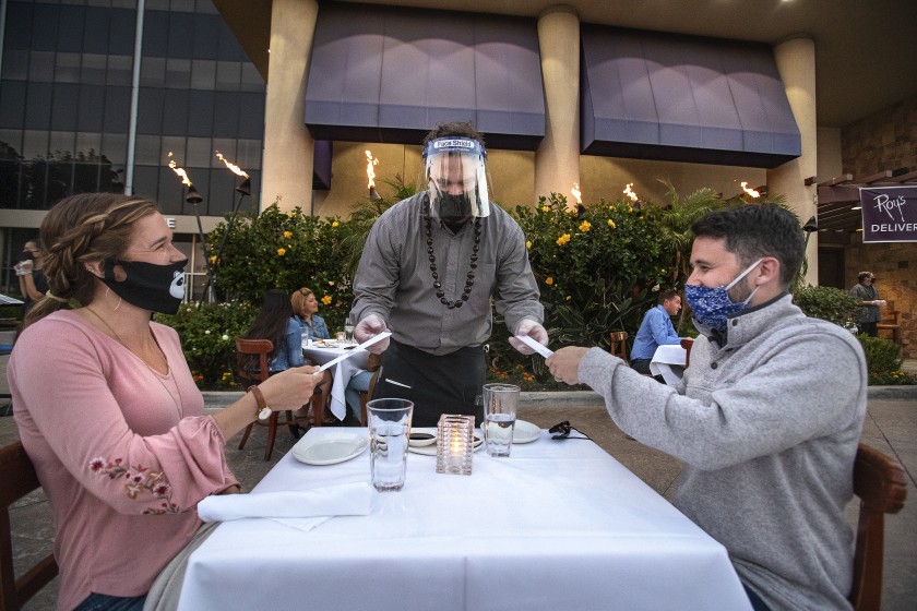 Jason Ruckart, managing partner at Roy’s restaurant in Woodland Hills, hands chopsticks to Nicole Lehning and her husband, Kyle, as they dine outdoors in what was previously the valet parking area.(Mel Melcon / Los Angeles Times)