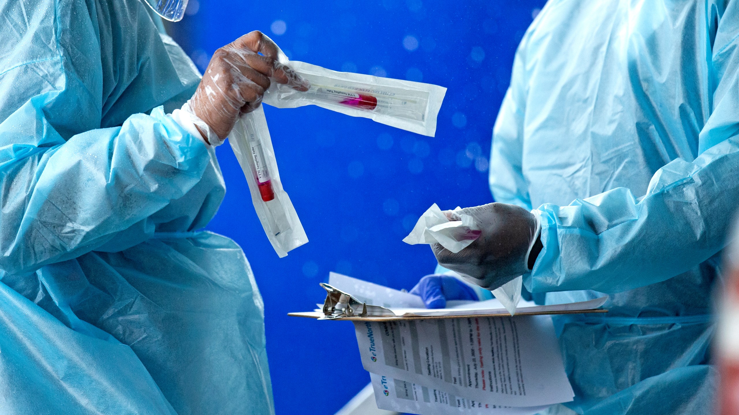 In this July 23, 2020 file photo, health care workers prepare a COVID-19 test sample before a person self-administered a test at the COVID-19 drive-thru testing center at Miami-Dade County Auditorium in Miami. (David Santiago/Miami Herald via AP)