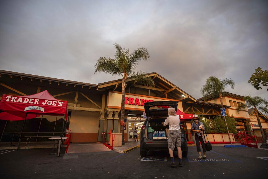 People load water into their car in front of a Trader Joe's grocery store as smoke from the Bobcat Fire rises in the background, Sunday, Sept. 6, 2020, in Azusa, Calif. (AP Photo/Christian Monterrosa)