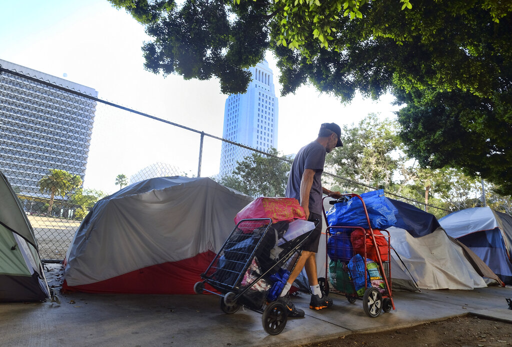 A homeless man moves his belongings from a street behind Los Angeles City Hall as crews prepared to clean the area on July 1, 2019. (Richard Vogel / Associated Press)