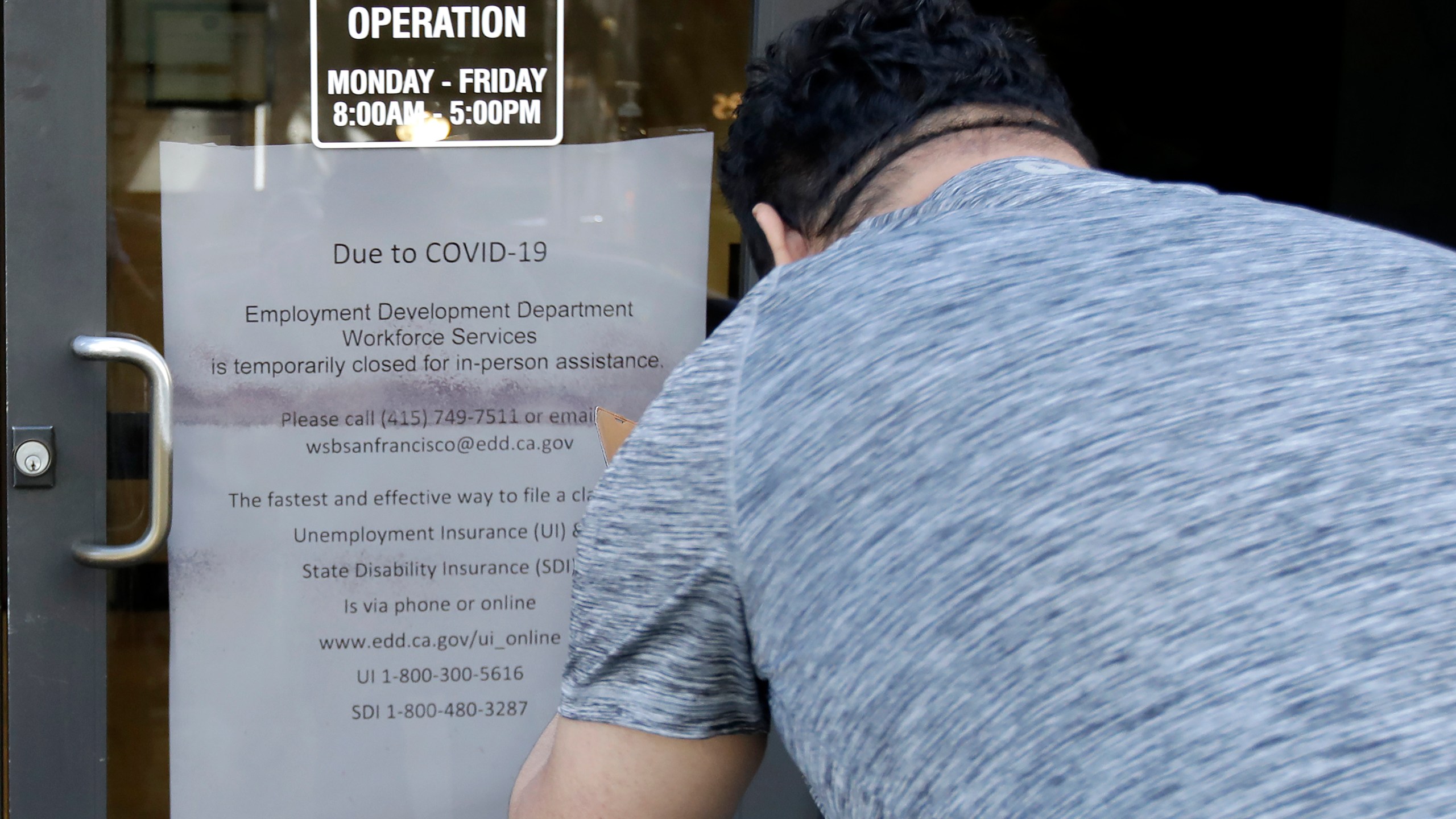 In this March 26, 2020 file photo, a man takes a photo of a sign advising that a Employment Development Department office in San Francisco is closed due to coronavirus concerns. (Jeff Chiu/Associated Press)