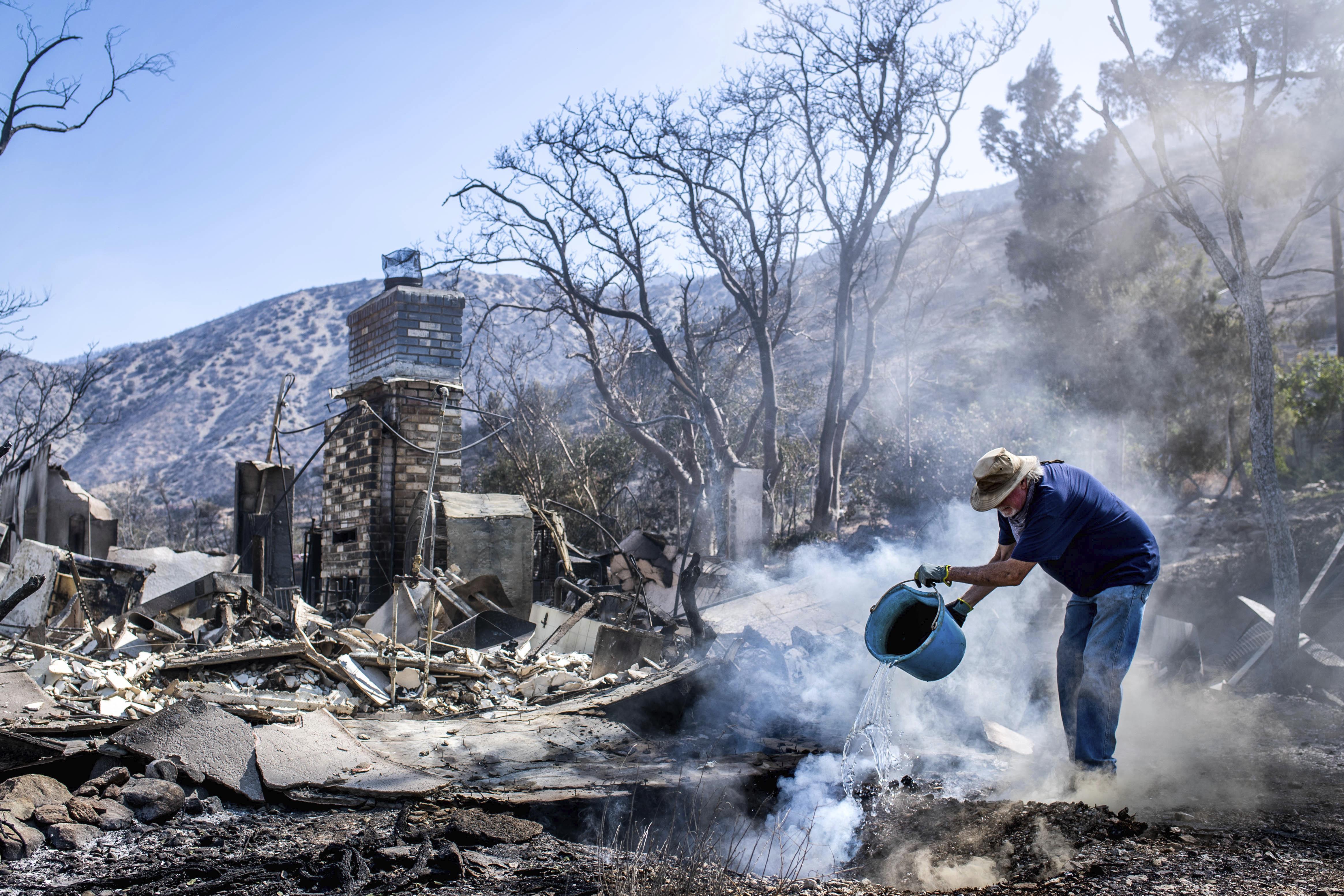 Dale Burton, of Leona Valley, tries to put out the fire that continues to smolder at his friend Cheryl Poindexter's property on Monday, Sept. 21, 2020, after the Bobcat Fire burned her home of 27 years and the 11-acre property where she ran an animal rescue in Juniper Hills. (Sarah Reingewirtz/The Orange County Register via AP)