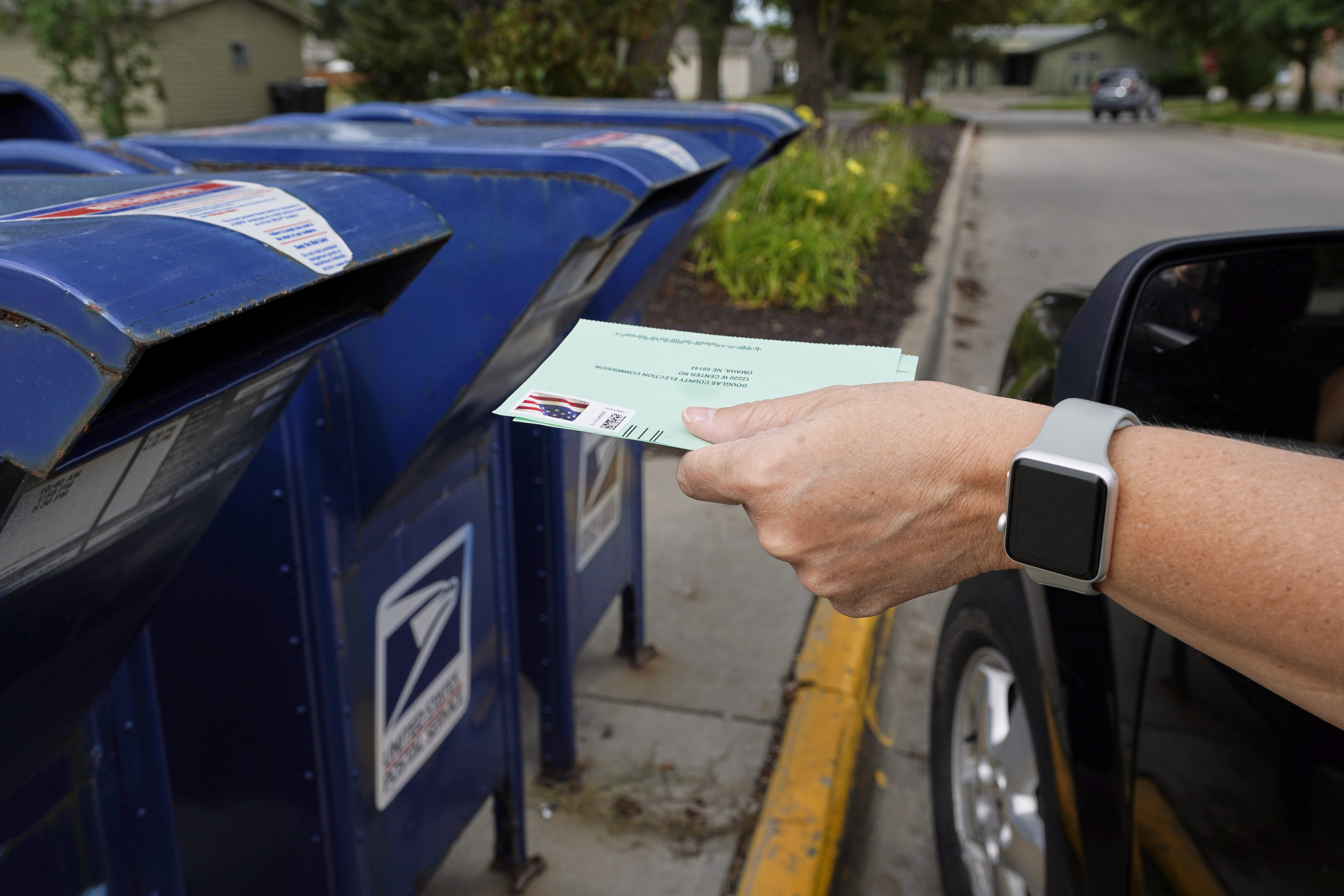 In this Tuesday, Aug. 18, 2020, file photo, a person drops applications for mail-in-ballots into a mailbox in Omaha, Neb. Data obtained by The Associated Press shows Postal Service districts across the nation are missing the agency’s own standards for on-time delivery as millions of Americans prepare to vote by mail. (AP Photo/Nati Harnik, File)