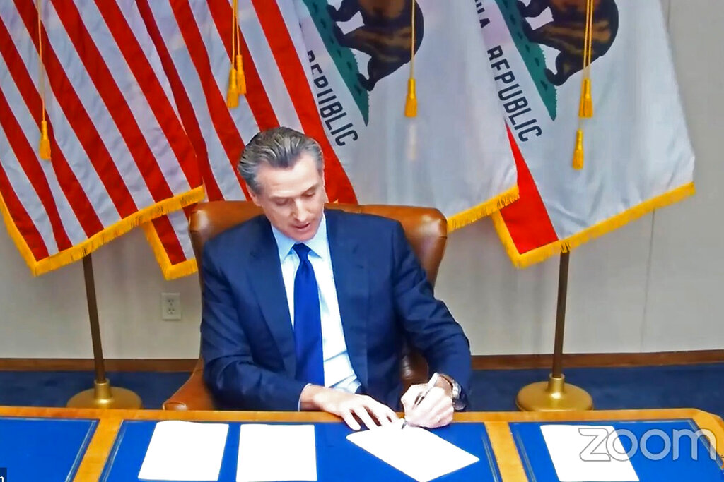 In this image taken during a video broadcast via Zoom, California Gov. Gavin Newsom signs a law on Sept. 25, 2020, in Sacramento that for the first time defines “medical necessity," a move aimed at requiring private health insurance plans to pay for more mental health and drug addiction treatments. (Zoom via AP)