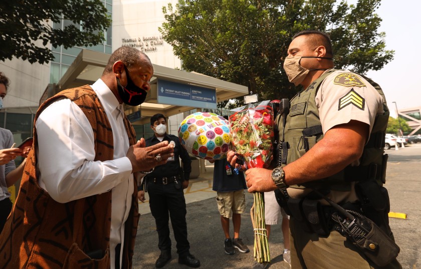 Community activist Najee Ali gives L.A. County sheriff’s Sgt. Larry Villareal flowers and a “get well” balloon outside the St. Francis Medical Center in Lynwood on Monday for the two deputies who were recovering from being shot in Compton.(Genaro Molina / Los Angeles Times)