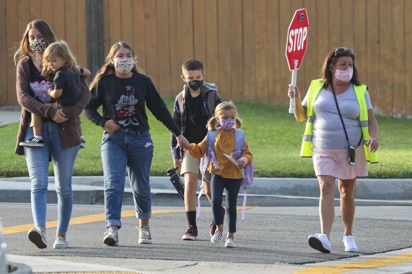 A crossing guard helps students as they return to in-class education, after months of closure due COVID-19 pandemic, at James H. Cox Elementary School in Fountain Valley.(Irfan Khan / Los Angeles Times)