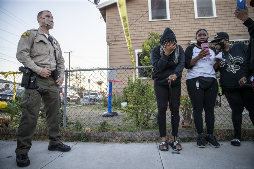 An L.A. County sheriff's deputy stands behind a caution tape as a group of mourners stand on the other side after the deputy killing of Dijon Kizzee in the Westmont neighborhood on Aug. 31, 2020. (Robert Gauthier / Los Angeles Times)