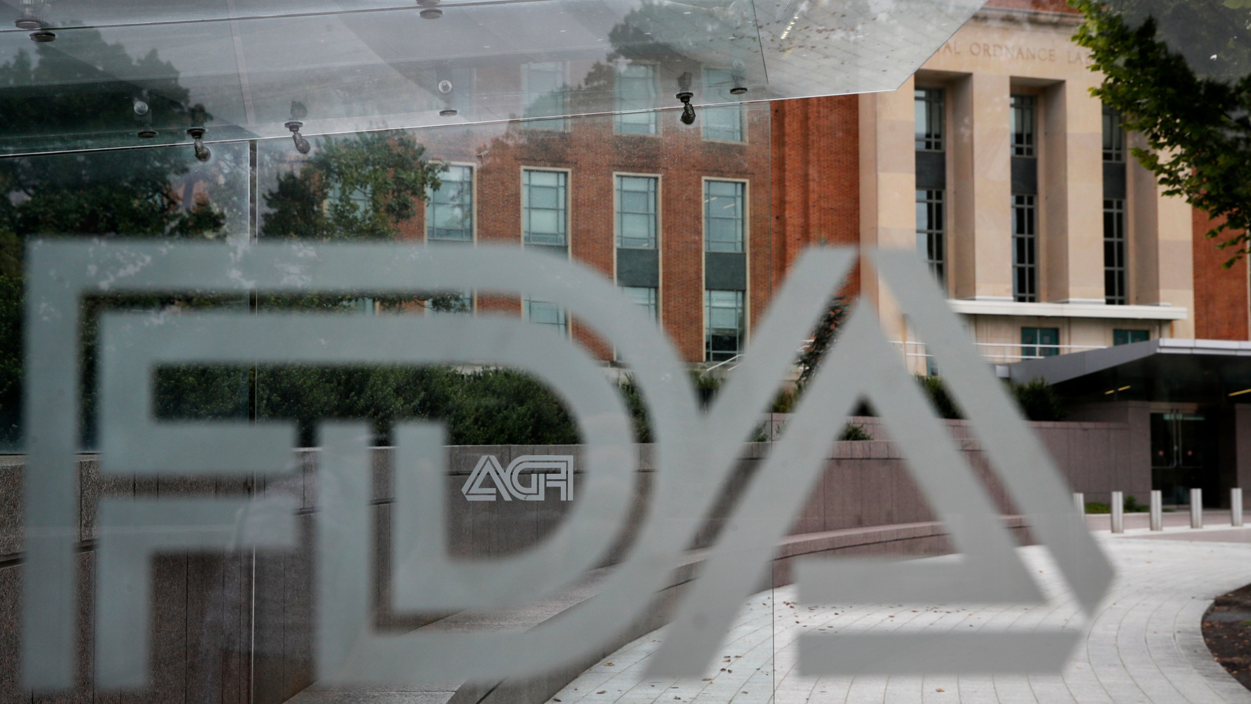 This Aug. 2, 2018, file photo shows the U.S. Food and Drug Administration building behind FDA logos at a bus stop on the agency's campus in Silver Spring, Md. In a report to Congress and an accompanying “playbook” for states and localities, key federal health agencies and the Defense Department sketched out complex plans for a vaccination campaign to begin gradually early next year or later in 2020, eventually ramping up to reach any American who wants a shot. The Pentagon is involved with the distribution of vaccines, but civilian health workers will be the ones giving shots. (AP Photo/Jacquelyn Martin, File)